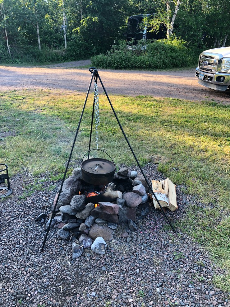 Using a tripod to hold a Dutch oven over a campfire to cook Jambalaya